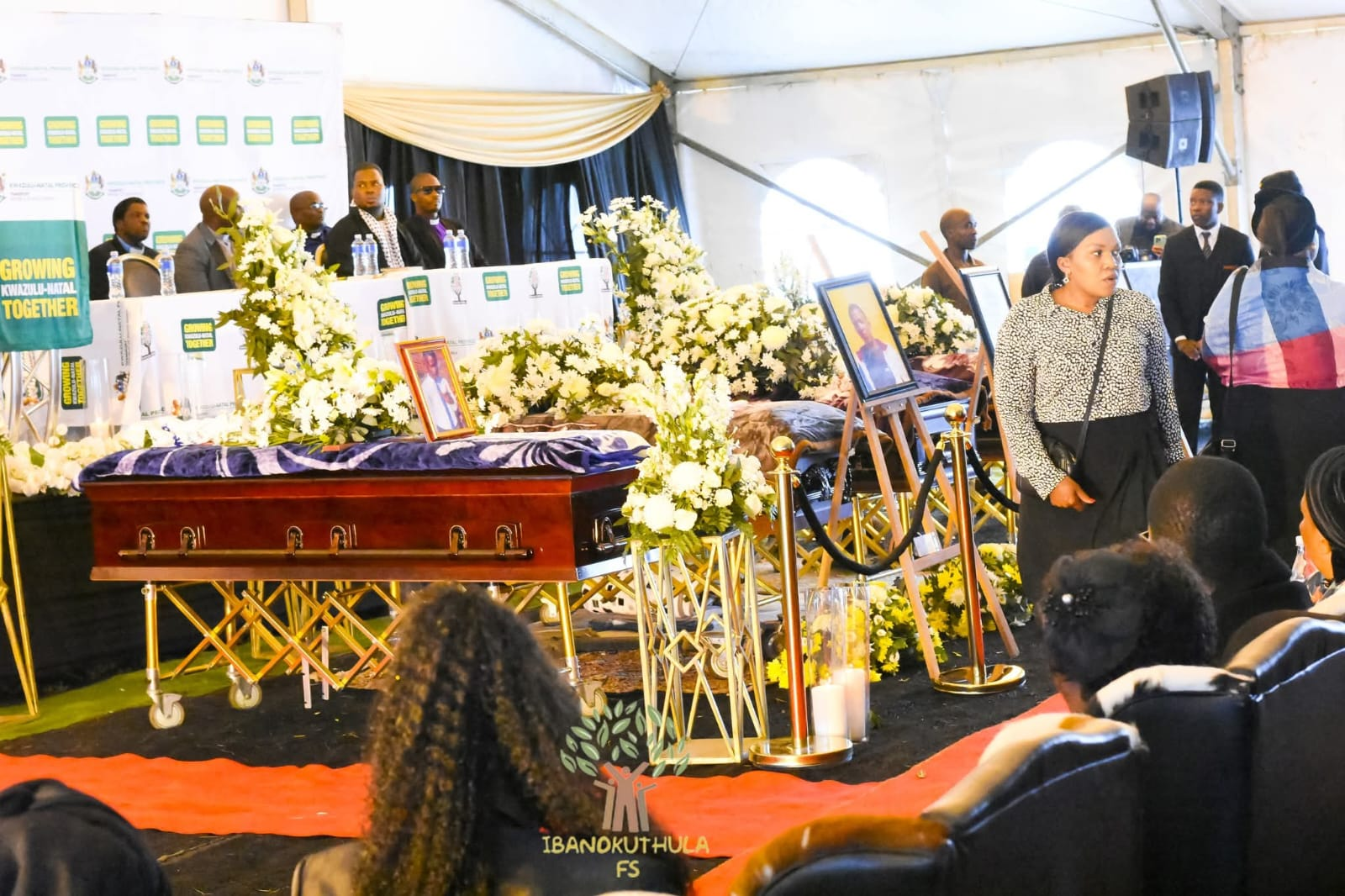 A funeral service arranged with flowers, framed portraits and a casket